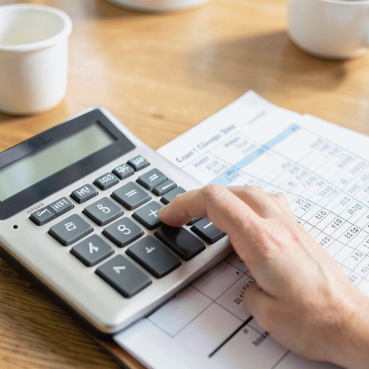 Hand calculating HPP using a calculator and spreadsheet on a desk, illustrating the process of determining selling price.