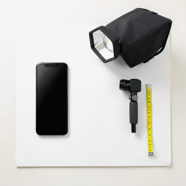 Tata letak datar (flat lay) berisi peralatan fotografi produk esensial untuk e-commerce, seperti smartphone, softbox, dan latar belakang putih, menunjukkan persiapan pemotretan profesional.